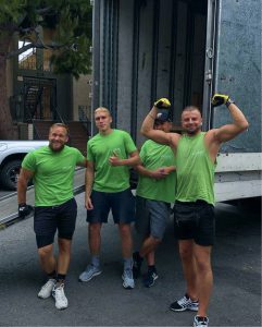 Four men in green shirts and shorts from Bay Area Movers are standing near an open truck. Two of them are posing with their arms flexed, while the other two are giving thumbs-up gestures.
