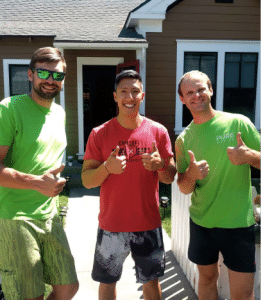 Three men standing outside a house, smiling and giving thumbs up. Two men are wearing green shirts, and the one in the middle is sporting a red shirt—a perfect representation of Bay Area movers celebrating another successful job.